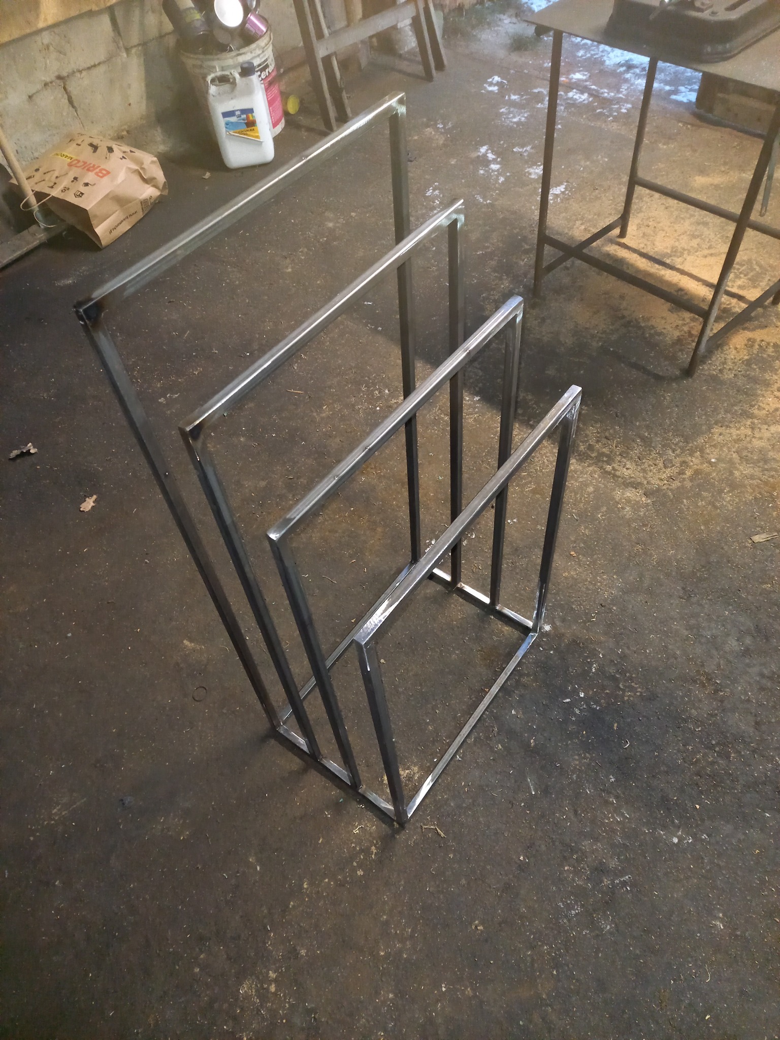 Metalowy stojak na ręczniki z profili kwadratowych, spawany, w surowym stanie, widoczne ślady obróbki i spawania, na tle warsztatu.
