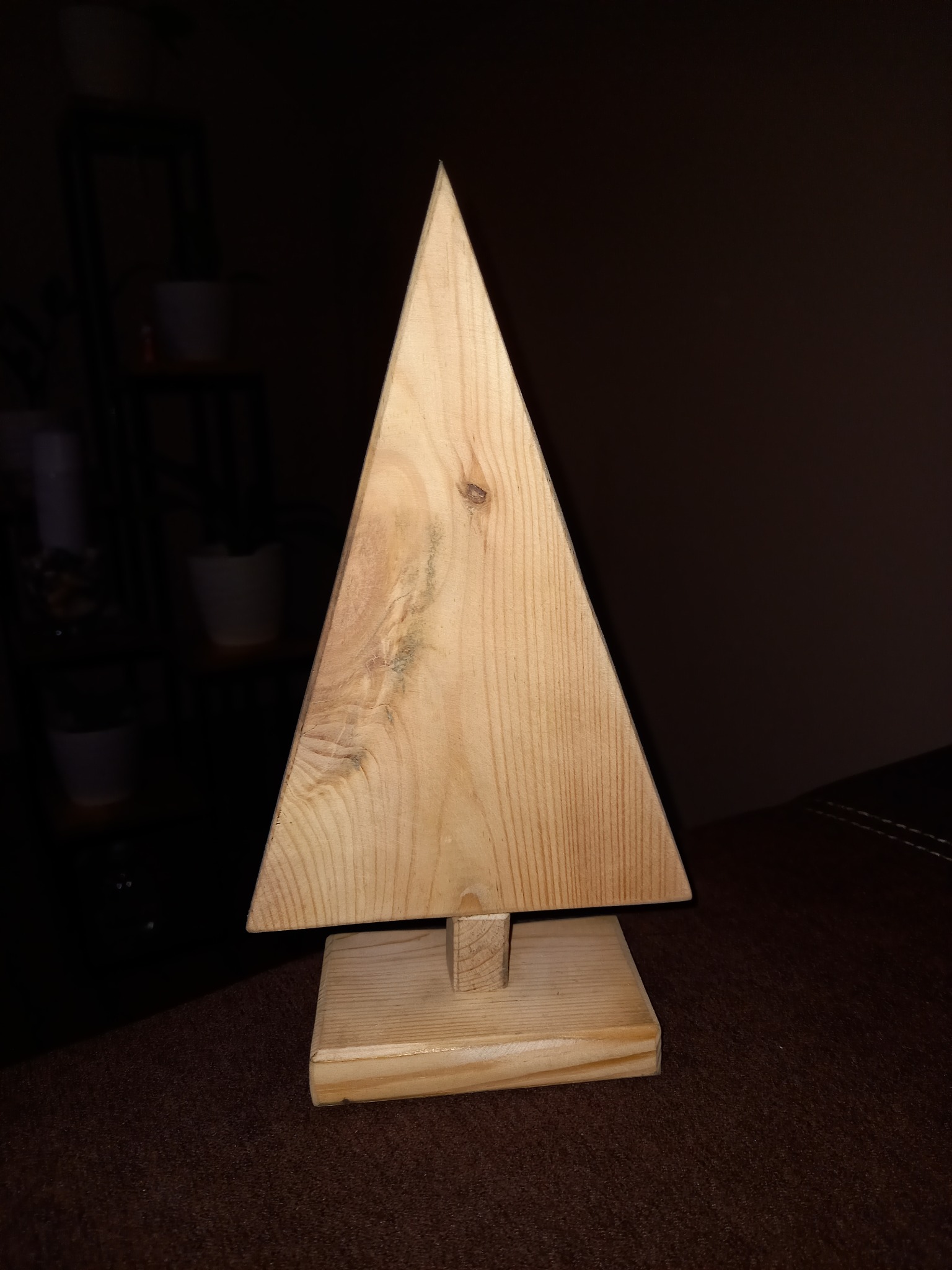 Drewniana choinka wykonana ręcznie, z widocznymi słojami i sękami, stojąca na podstawie z ciemnym tłem.