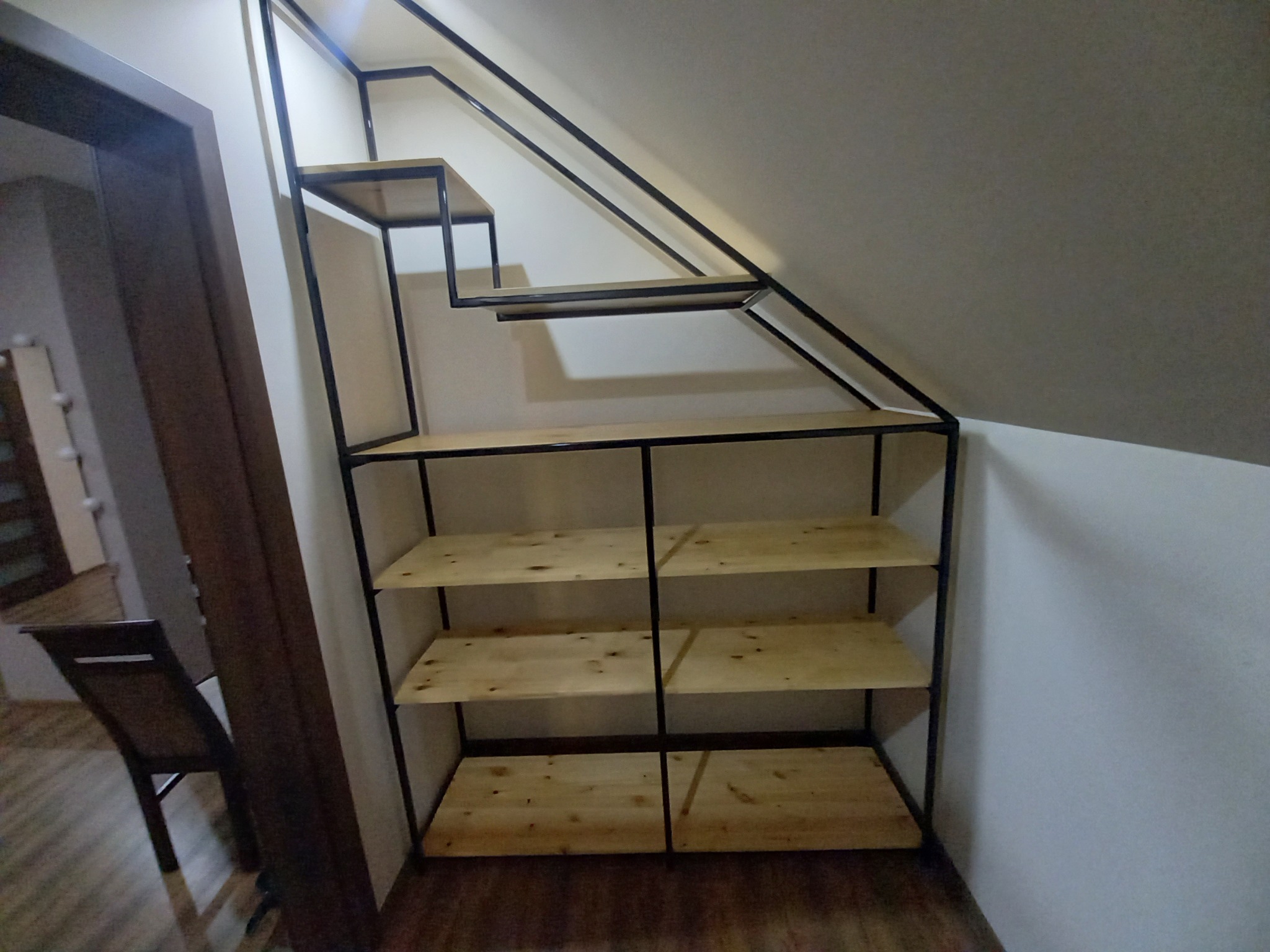 Metalowa konstrukcja schodów z drewnianymi półkami wkomponowana w skos dachu, widok z dołu na schody z półkami.