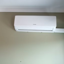 INSTALACJE Zabrze-Gliwice - Biały klimatyzator Sinclair zamontowany na ścianie w jasnym pomieszczeniu, widoczny przewód odprowadzający, minimalistyczny design.