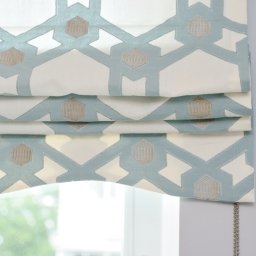 Homelytextile - Złożona roleta rzymska w kolorze biało-błękitnym z geometrycznym wzorem, zamontowana w oknie, z widocznym łańcuszkiem sterującym.