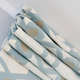 Homelytextile - Złożona, pastelowa roleta okienna z geometrycznym wzorem w odcieniach błękitu, beżu i bieli, zamontowana na karniszu.