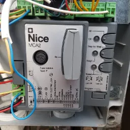 Panel sterowania Nice MCA2 z podłączonymi przewodami, widoczne złącza, bezpiecznik i przyciski funkcyjne.