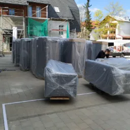 Meble zapakowane w folię ochronną, przygotowane do transportu, na tle budynku w trakcie budowy, z widocznym rusztowaniem i busem z napisem 'Stobrawa.pl'.