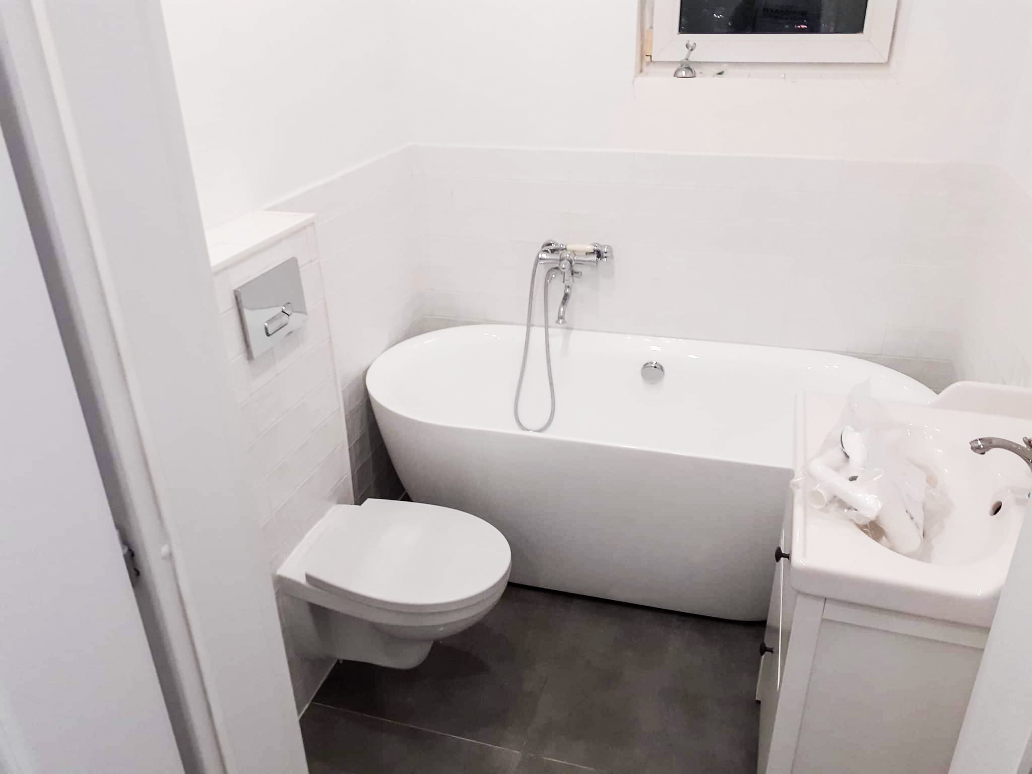 Nowoczesna, biała łazienka z wolnostojącą wanną, umywalką z szafką i podwieszanym WC, widok z perspektywy drzwi.