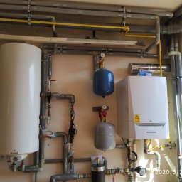 R.P.S-Studio - Kaskada instalacji centralnego ogrzewania z kotłem gazowym De Dietrich, zasobnikiem Galmet, pompami obiegowymi i zbiornikami wyrównawczymi, widoczne rury instalacyjne z zaworami i manometrami.