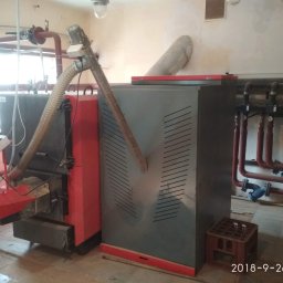 R.P.S-Studio - Kotłownia z dwoma kotłami na paliwo stałe, widoczne rury instalacji centralnego ogrzewania, skrzynka na podłodze.