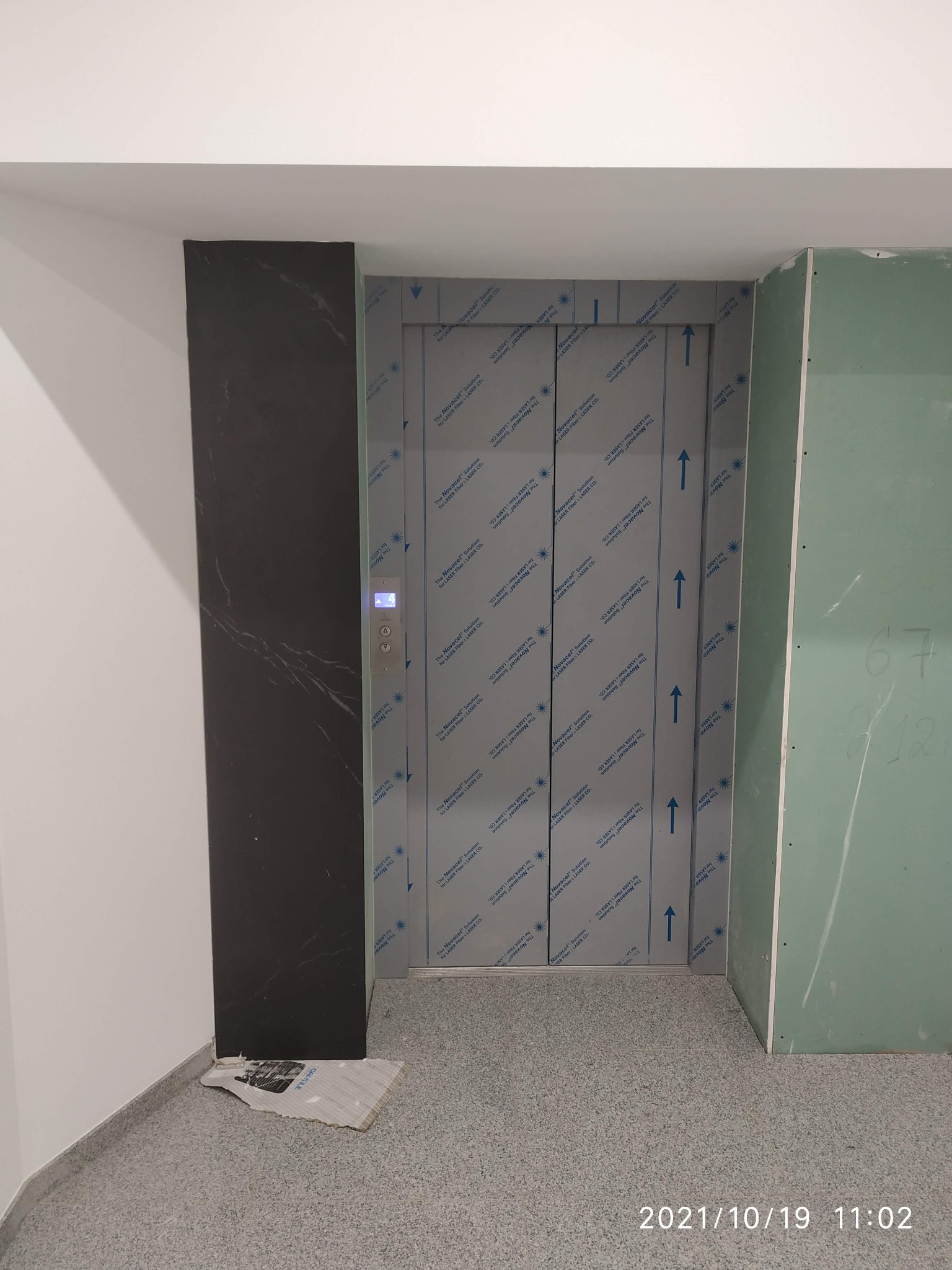 Wnętrze w trakcie wykańczania: obudowa szybu windowego z czarnego marmuru, drzwi windy zabezpieczone folią ochronną, ściana z płyty karton-gips przed szpachlowaniem.