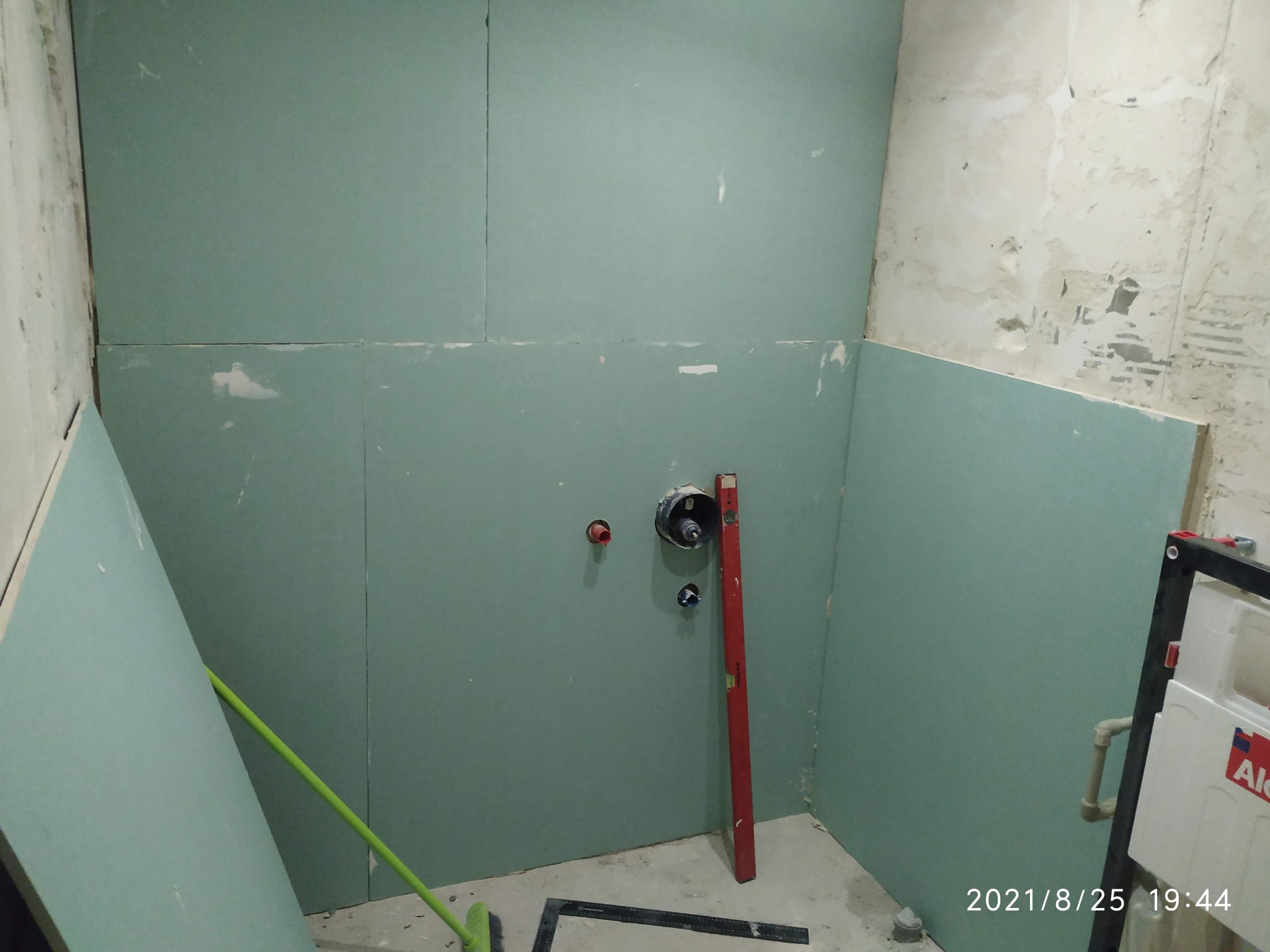 Przygotowanie łazienki do dalszych prac: ściany wyłożone płytami gipsowo-kartonowymi, widoczne punkty instalacji hydraulicznej oraz poziomica oparta o ścianę.