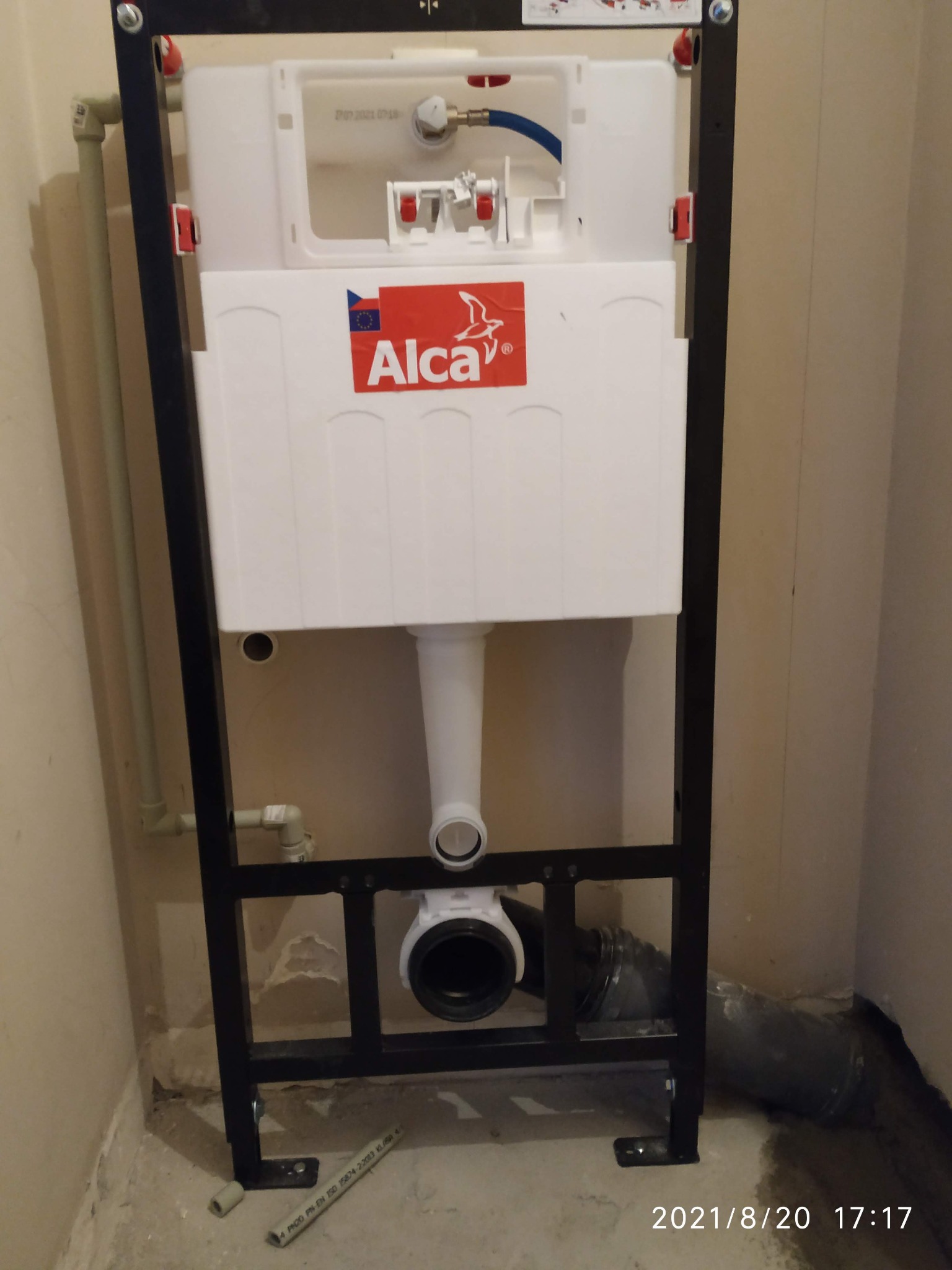 Stelaż podtynkowy WC marki Alca zamontowany w surowym stanie, widoczne podłączenia hydrauliczne i rura kanalizacyjna w ścianie.