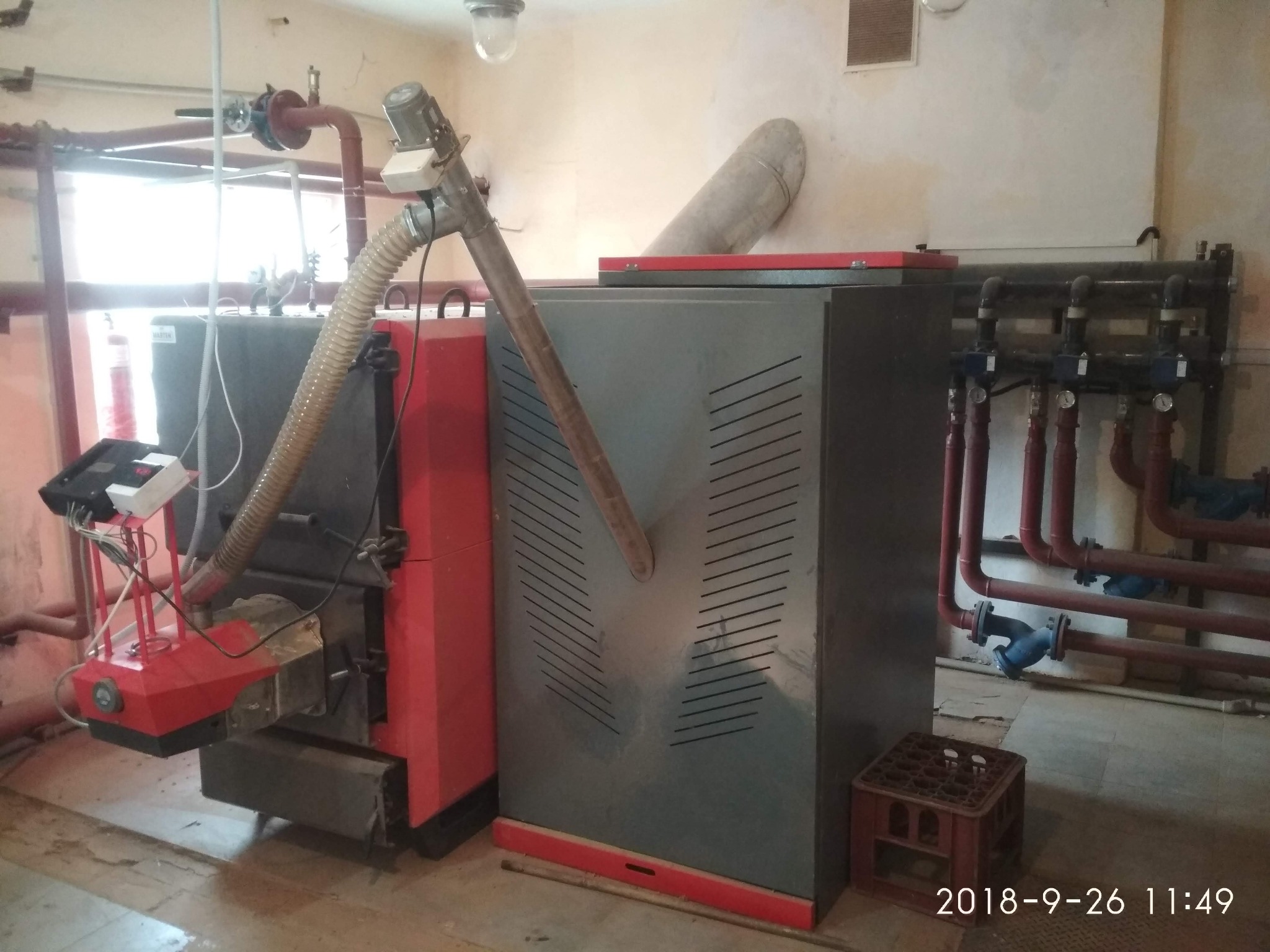 Kotłownia z dwoma kotłami na paliwo stałe, widoczne rury instalacji centralnego ogrzewania, skrzynka na podłodze.