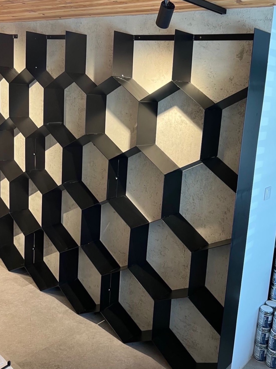 Metalowa konstrukcja w kształcie plastra miodu, czarne obramowanie, szare wypełnienie, oświetlenie punktowe, nowoczesny design, widok z boku.