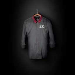 Szara koszula z bordowym kołnierzykiem i mankietami, wisząca na drewnianym wieszaku na tle czarnej ściany. Na koszuli widoczne logo restauracji 'Do LuCasa'.