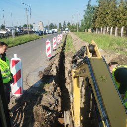 Bamber FV Kamil Kaczmarski - Wykop liniowy pod instalacje, zabezpieczony słupkami ostrzegawczymi. Żółta koparka BamBer w trakcie pracy, dwóch pracowników w odblaskowych kamizelkach nadzoruje wykop.