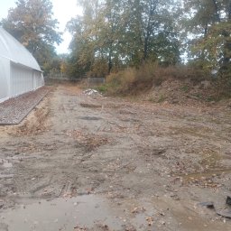 Bamber FV Kamil Kaczmarski - Błotnisty teren po robotach ziemnych z widocznymi śladami opon, kałużami i liśćmi. W tle biała hala namiotowa i drzewa.