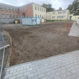 Bamber FV Kamil Kaczmarski - Przygotowany teren pod budowę z kontenerem biurowym, ogrodzeniem i chodnikiem z kostki. Widoczny budynek w tle i hydrant.