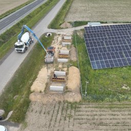 Bamber FV Kamil Kaczmarski - Wylewanie betonu pod fundamenty paneli słonecznych w Chociszewie. Widok z góry na betonowóz i wykopane doły z szalunkami. Prace ziemne w toku.