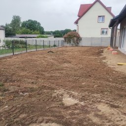 Bamber FV Kamil Kaczmarski - Przygotowany teren pod budowę domu jednorodzinnego. Widoczne ślady opon po maszynach budowlanych, ogrodzenie panelowe i budynki w tle.