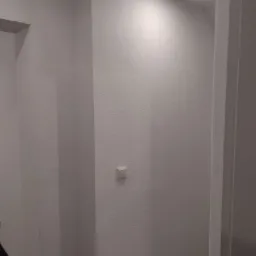 Świeżo pomalowane na biało wnętrze, widoczny fragment korytarza z włącznikiem światła i punktowym oświetleniem sufitowym, ukazujący fakturę ściany.