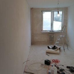Firma Cyprian - Pokój w trakcie prac przygotowawczych: ściany po nałożeniu gładzi, okno zabezpieczone folią, drabina oparta o ścianę, na podłodze rozłożone narzędzia i materiały.