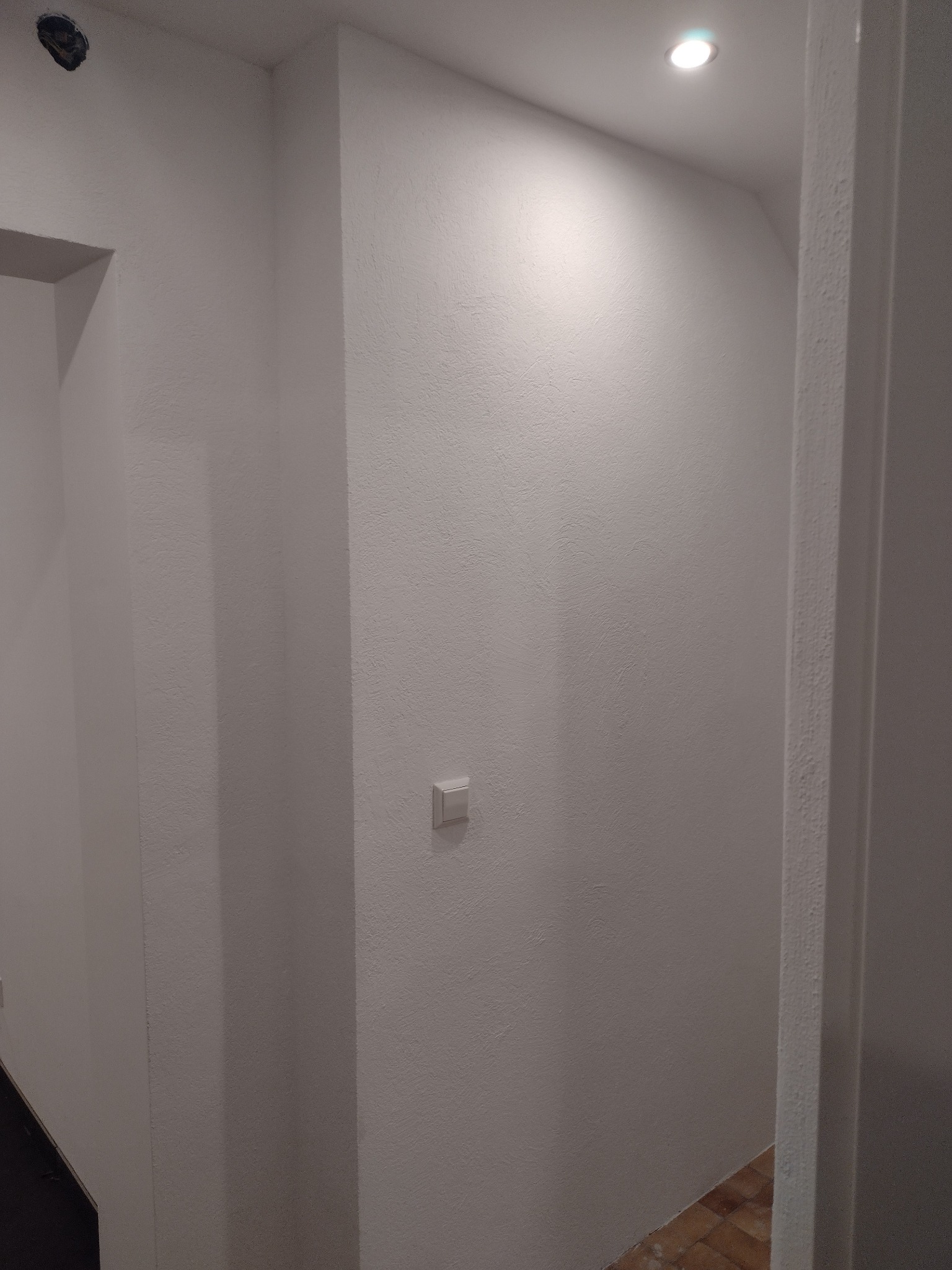 Świeżo pomalowane na biało wnętrze, widoczny fragment korytarza z włącznikiem światła i punktowym oświetleniem sufitowym, ukazujący fakturę ściany.