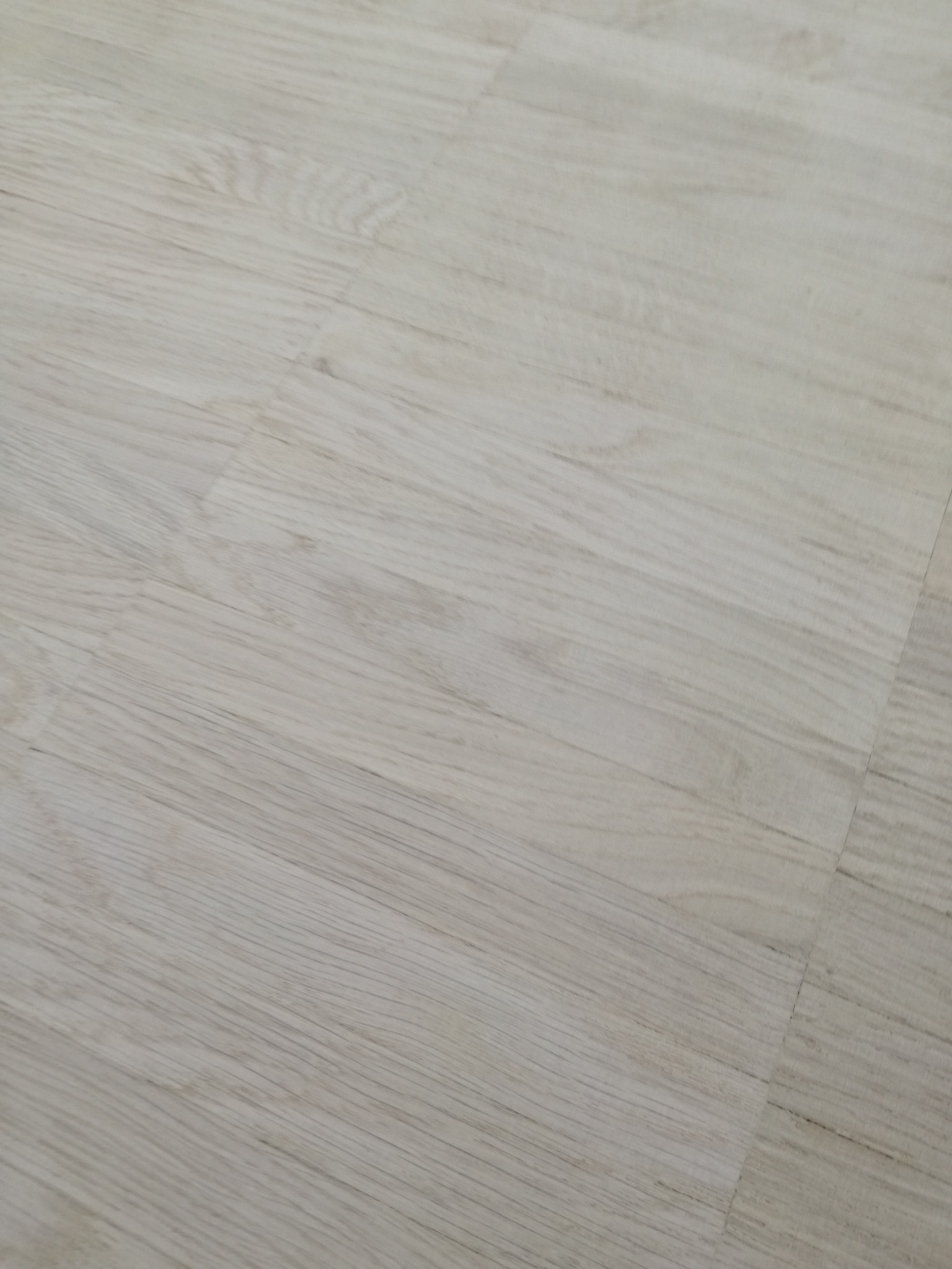 Jasny, parkiet ułożony z paneli o delikatnym rysunku drewna, widoczne łączenia między panelami.