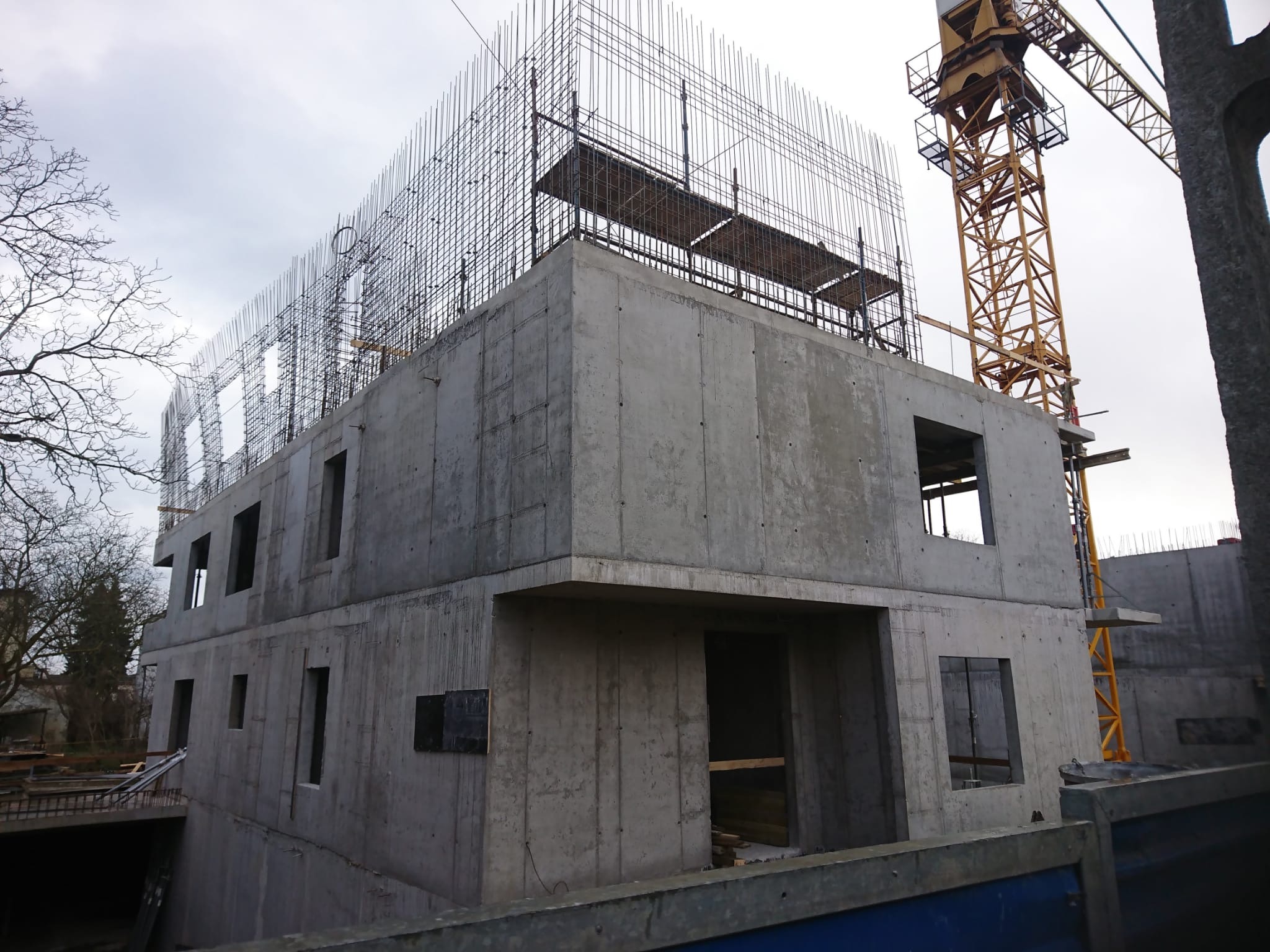 Surowy stan budynku z betonu w Gdyni, widoczne zbrojenia na dachu i żółty dźwig w tle, Cyprysowa.