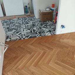 Dmytro Vlasov Sova VDV - Ułożona podłoga z parkietu w jodełkę sąsiadująca z wzorzystą, czarno-białą posadzką. Widoczne materiały budowlane i instalacje.