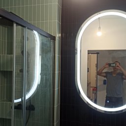 Dmytro Vlasov Sova VDV - Nowoczesna łazienka z kabiną prysznicową i okrągłym lustrem z podświetleniem LED. Ściany wyłożone zielonymi i czarnymi płytkami wertykalnymi. Widoczne odbicie osoby robiącej zdjęcie.