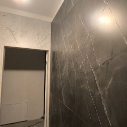 Dmytro Vlasov Sova VDV - Ciemna, marmurowa okładzina ścienna z białymi żyłami w łazience, widok na otwarte drzwi i fragment ściany z jasnymi płytkami imitującymi marmur.