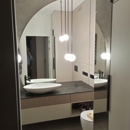 Dmytro Vlasov Sova VDV - Nowoczesna łazienka z owalnym lustrem, wiszącą umywalką na blacie z ciemnego kamienia i trzema kulistymi lampami wiszącymi na czarnych przewodach.