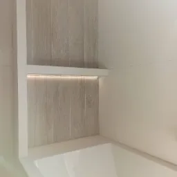 Półka wnękowa z podświetleniem LED nad wanną, wykończona płytkami imitującymi drewno.