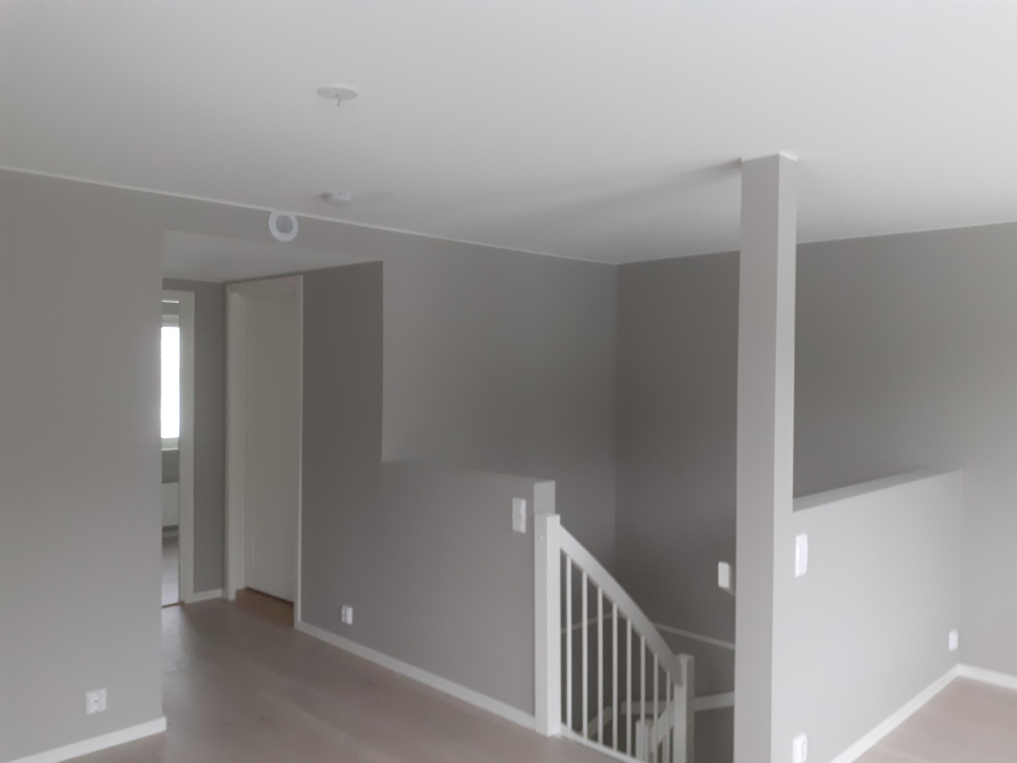 Wnętrze domu po remoncie: ściany pomalowane na szaro, białe schody i listwy przypodłogowe, widok na przedpokój z oknem.