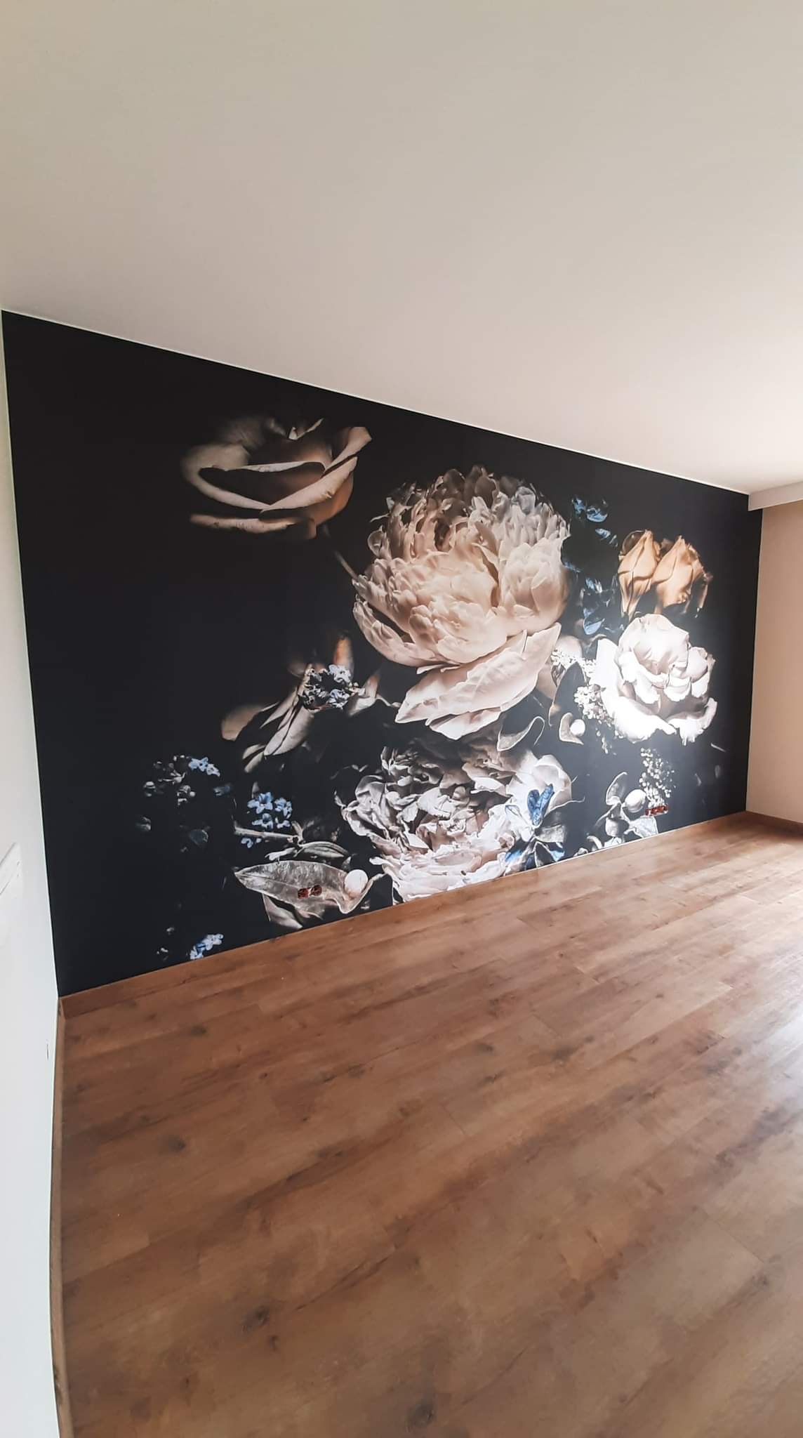 Pokój z fototapetą przedstawiającą bukiet kwiatów w stylu vintage na ciemnym tle, brązowa podłoga z paneli.