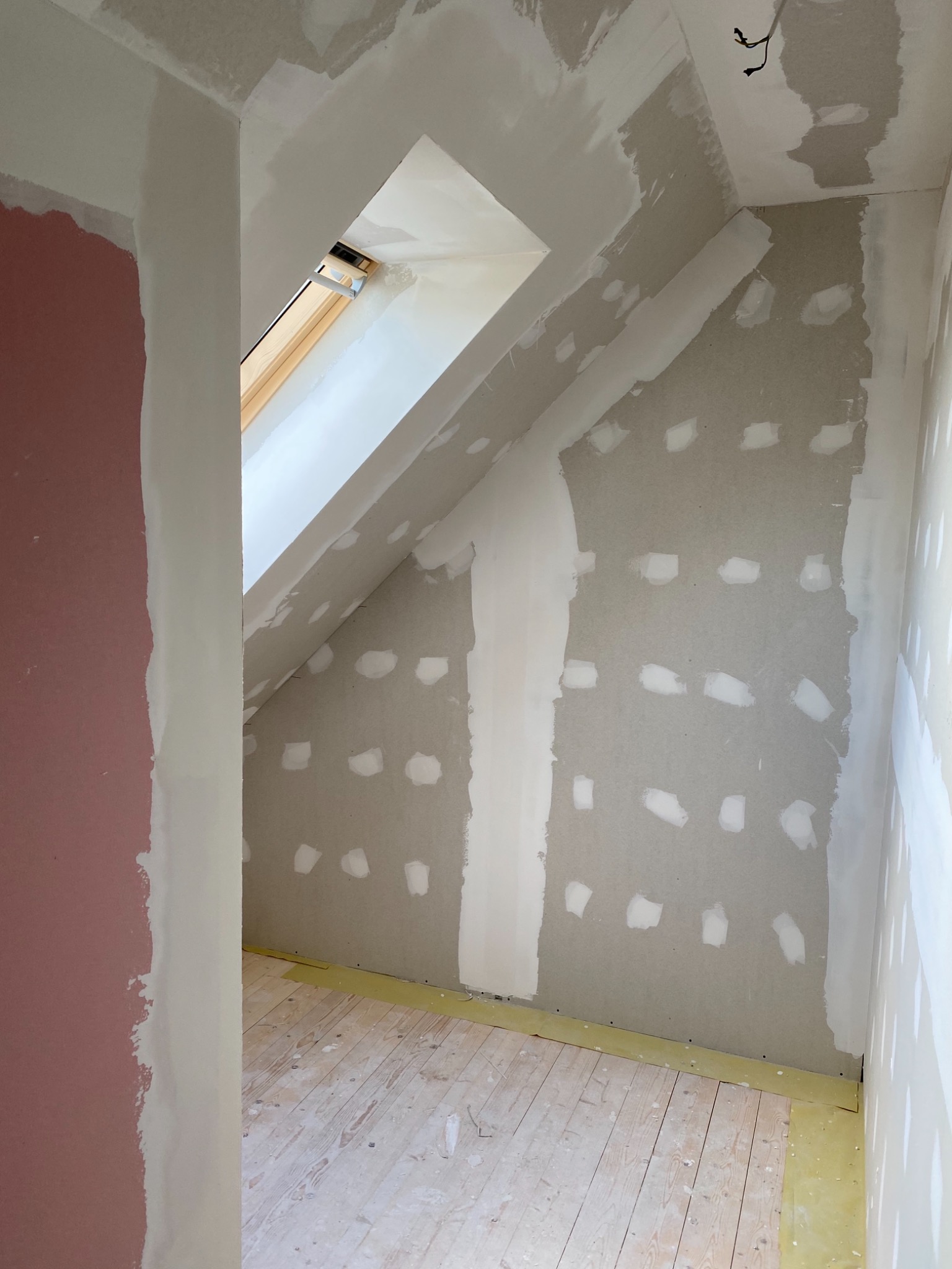 Poddasze w trakcie wykańczania: płyta karton gips z widocznymi miejscami po wkrętach, wstępnie zaszpachlowane, okno dachowe, zabezpieczona podłoga parkietowa.