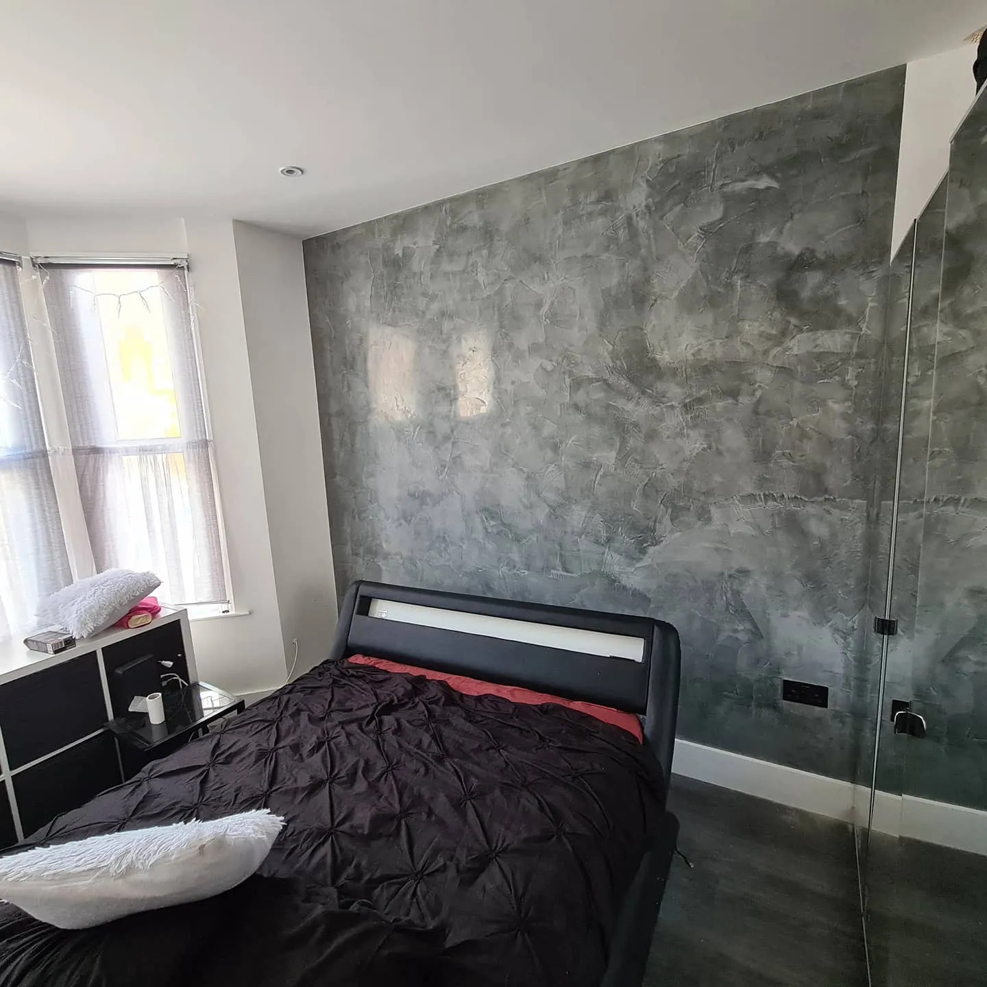 Sypialnia z łóżkiem i ścianą pokrytą dekoracyjną szarą fakturą imitującą beton, widok na ścianę z bliska.