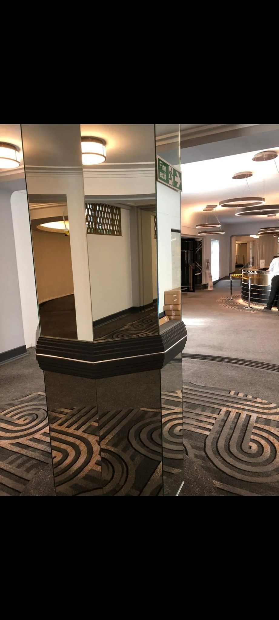 Wykończone wnętrze biura z lustrzanym filarem i wzorzystą wykładziną podłogową w stylu art deco.