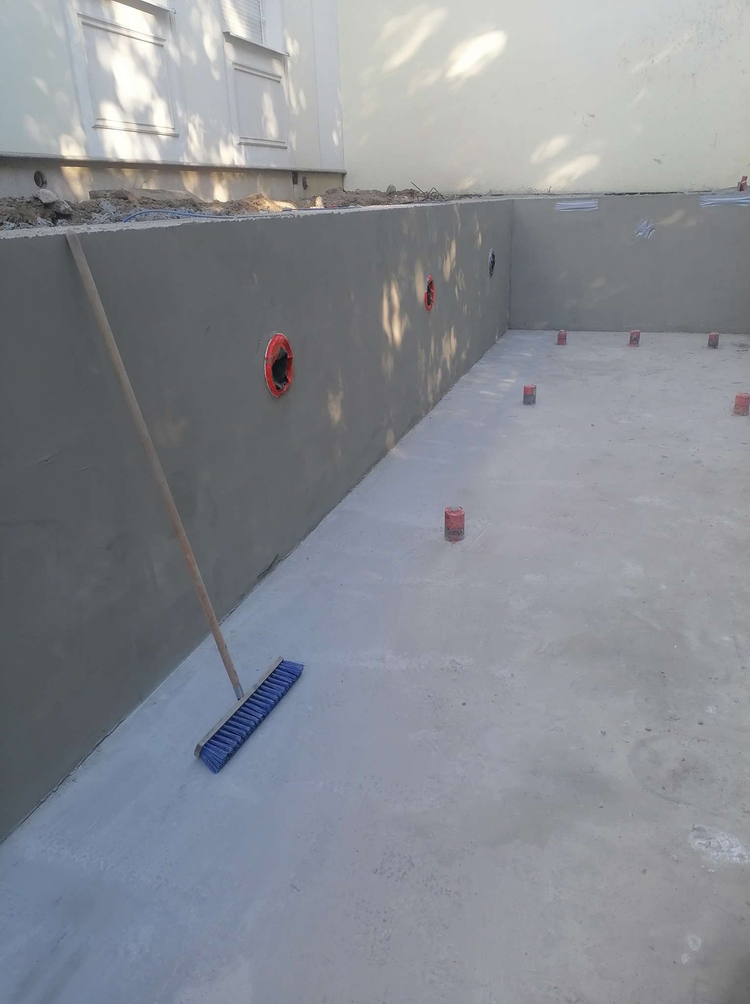 Wnętrze betonowego basenu w trakcie budowy, z widocznymi otworami na instalacje i szczotką opartą o ścianę. Widoczne podpory pod przyszłą konstrukcję.