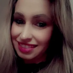 Portret uśmiechniętej kobiety z kolczykiem w nosie, pomalowanymi ustami w kolorze fuksji i blond włosami z ciemnymi odrostami.