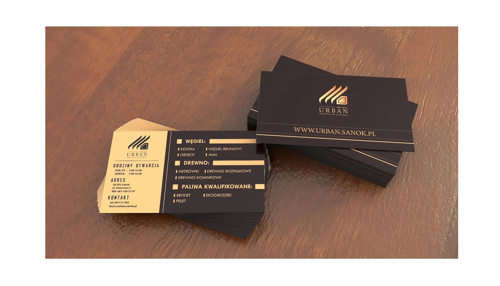 Stos wizytówek firmy Urban Przemysław Koczęra, z informacjami o godzinach otwarcia, adresie, kontakcie oraz asortymencie węgla i drewna opałowego, na drewnianym tle.