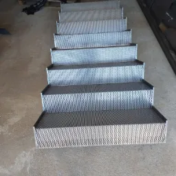 Metalowe schody ażurowe z perforowanej blachy, widok z góry w warsztacie, surowy beton na podłodze.