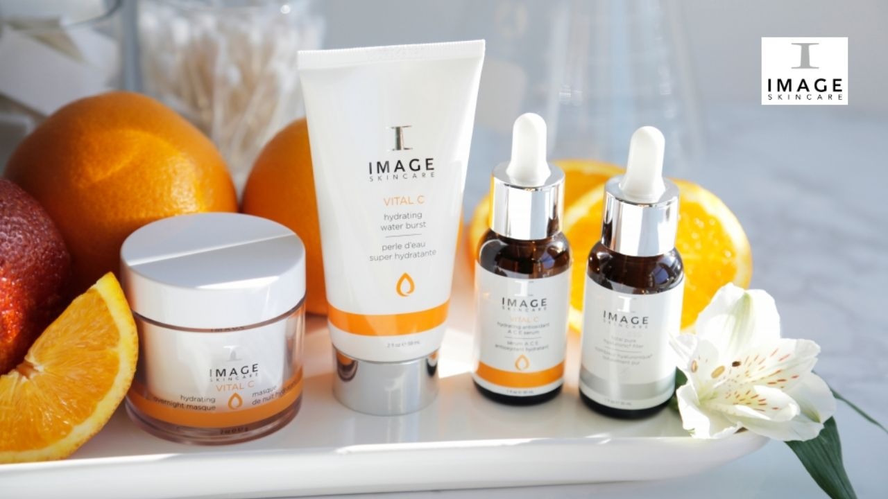 Zestaw kosmetyków IMAGE SKINCARE Vital C na białej tacy, otoczony cytrusami i białym kwiatem lilii, prezentacja produktów nawilżających do pielęgnacji skóry.