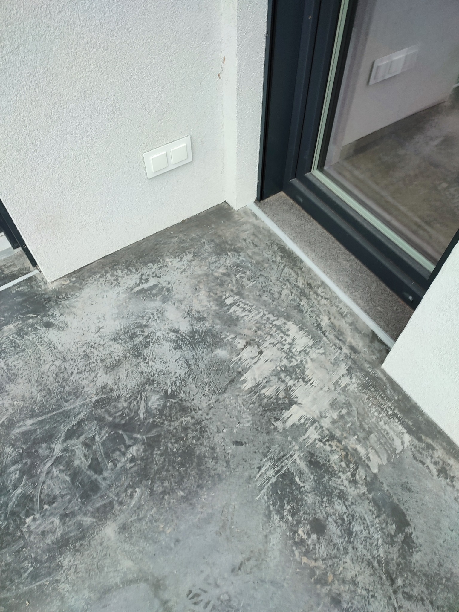 Przygotowanie podłoża pod panele: szlifowana wylewka samopoziomująca w rogu pomieszczenia z białymi ścianami i włącznikiem światła, widoczna rama okienna.