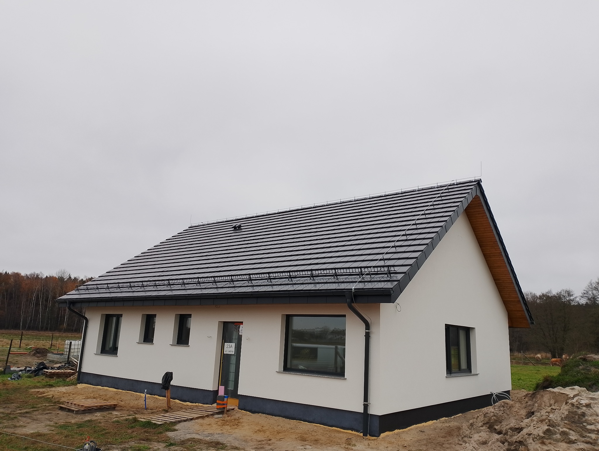 Nowoczesny dom jednorodzinny w Strzeleczkach z białą elewacją i ciemną dachówką. Widoczne detale wykończenia i otoczenie budynku.