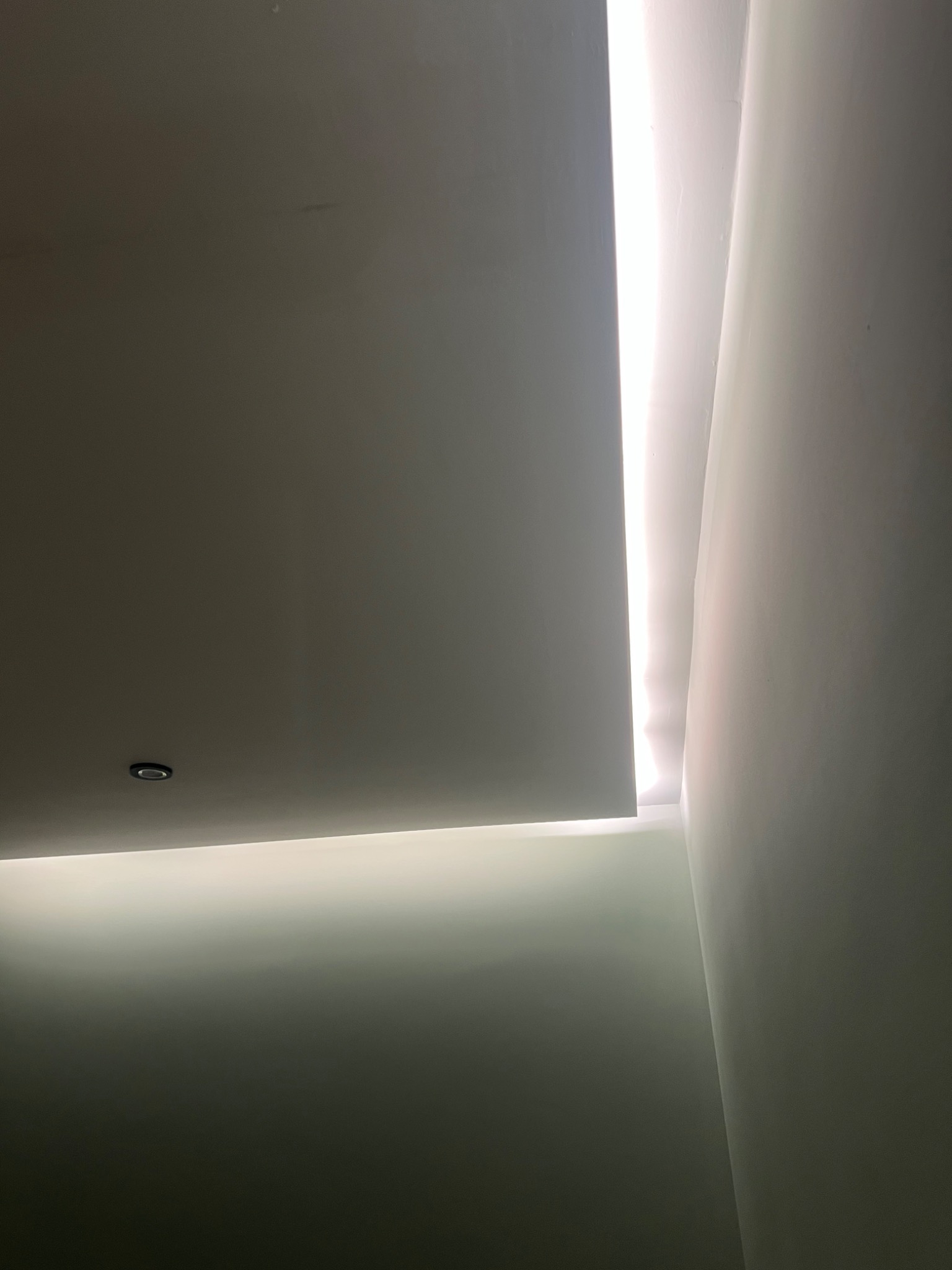 Nowoczesny sufit podwieszany z ukrytym oświetleniem LED, widoczna struktura ściany i punktowe oświetlenie.