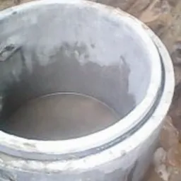 Betonowy krąg studzienny częściowo zagłębiony w ziemi, wypełniony wodą, widok z góry.