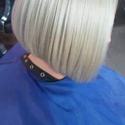 Krótkie, platynowe blond włosy w stylu bob, widoczne z tyłu, po strzyżeniu we Włocławku, z niebieską peleryną ochronną.