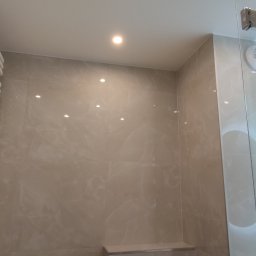 BM Construction - Nowoczesna łazienka z beżowymi płytkami imitującymi marmur, grzejnikiem drabinkowym, okrągłym lustrem z podświetleniem LED i szklaną kabiną prysznicową.