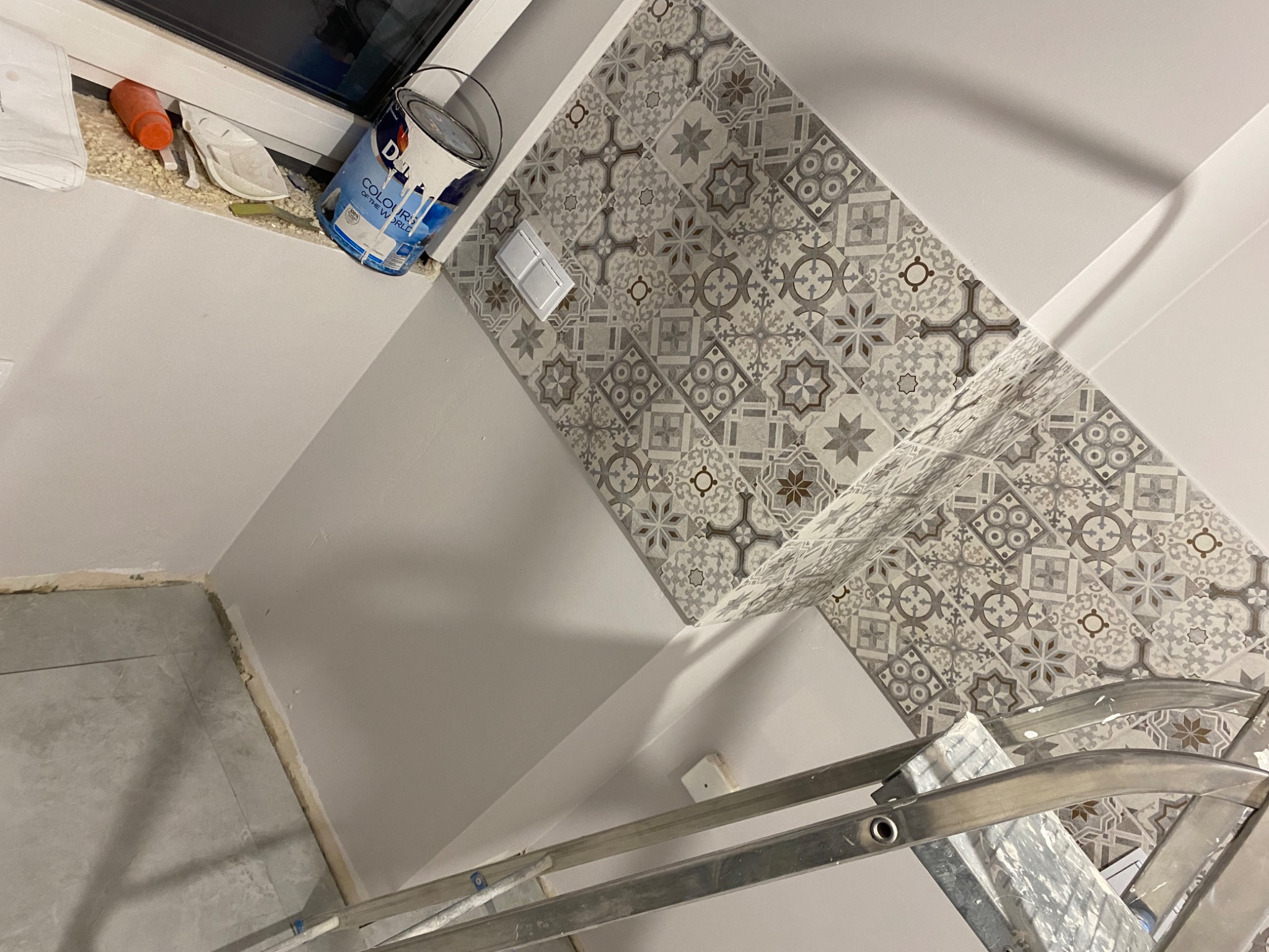 Świeżo pomalowana ściana w Miastkowie, z dekoracyjnymi płytkami u góry, widoczna puszka z farbą i drabina, sugerujące trwający proces odnawiania wnętrza.