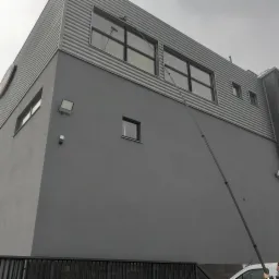 Mycie okien na wysokości w budynku o szarej elewacji z użyciem długiej lancy teleskopowej z zamontowaną szczotką i spryskiwaczem.